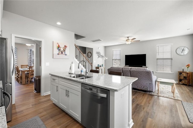 kitchen with appliances with stainless steel finishes, sink, white cabinets, a kitchen island with sink, and light stone countertops