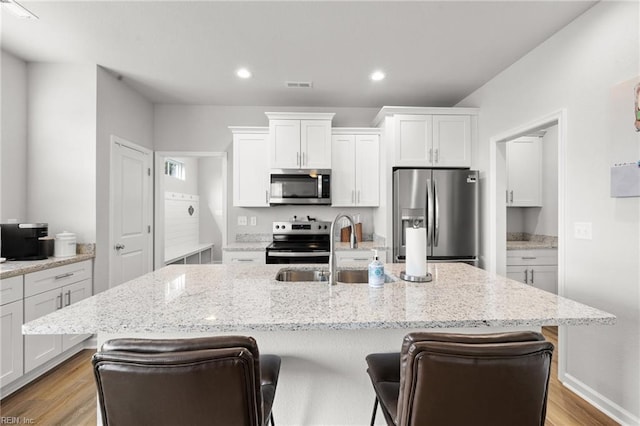 kitchen with a breakfast bar, white cabinetry, light stone counters, a center island with sink, and appliances with stainless steel finishes