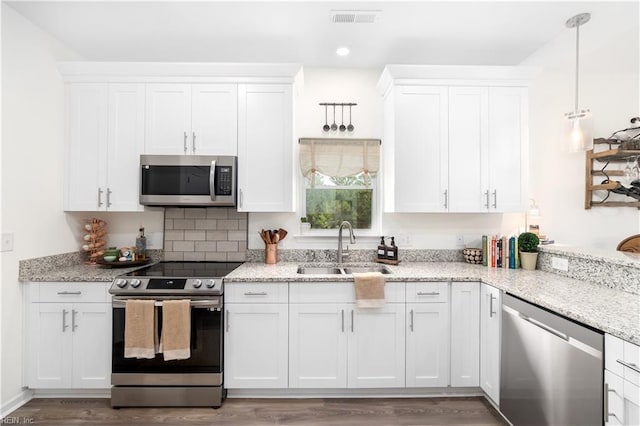 kitchen featuring sink, white cabinetry, light stone counters, decorative light fixtures, and appliances with stainless steel finishes