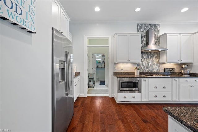 kitchen featuring white cabinetry, wall chimney range hood, dark stone counters, and appliances with stainless steel finishes