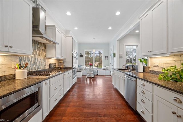 kitchen with white cabinetry, appliances with stainless steel finishes, dark stone counters, and wall chimney range hood