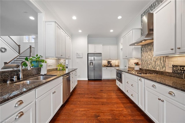 kitchen featuring sink, appliances with stainless steel finishes, white cabinetry, dark stone countertops, and wall chimney exhaust hood