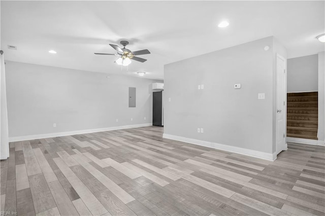 unfurnished room featuring a wall mounted air conditioner, electric panel, ceiling fan, and light hardwood / wood-style floors