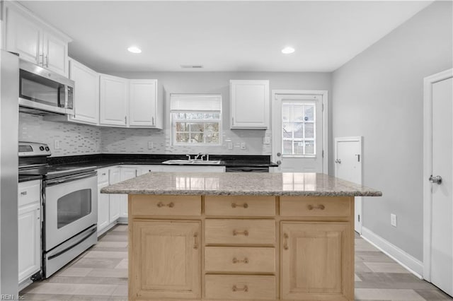 kitchen featuring stainless steel appliances, white cabinetry, a center island, and sink