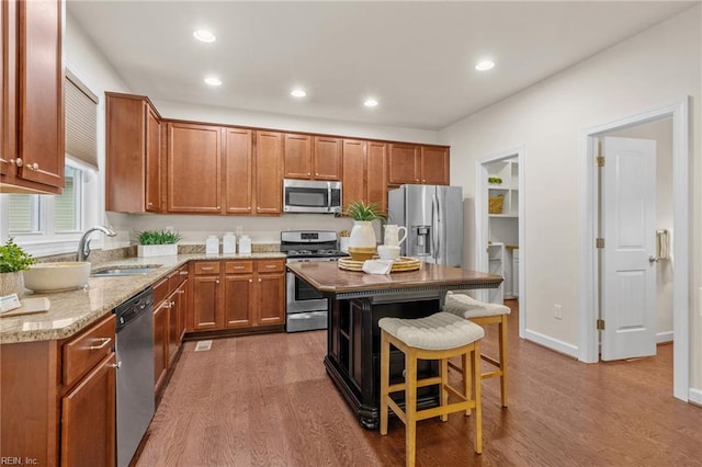 kitchen featuring stainless steel appliances, brown cabinetry, a sink, and a center island