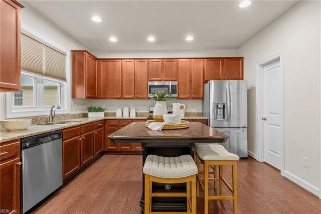 kitchen with appliances with stainless steel finishes, a sink, light stone counters, and wood finished floors