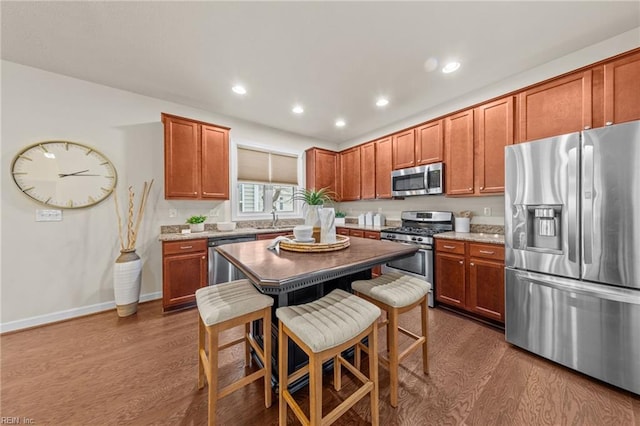 kitchen featuring dark wood finished floors, a breakfast bar area, stainless steel appliances, brown cabinetry, and a kitchen island