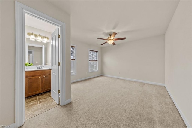 spare room featuring light carpet, ceiling fan, a sink, and baseboards