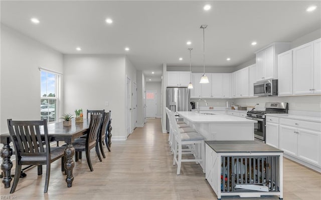 kitchen featuring sink, white cabinetry, pendant lighting, stainless steel appliances, and a kitchen island with sink