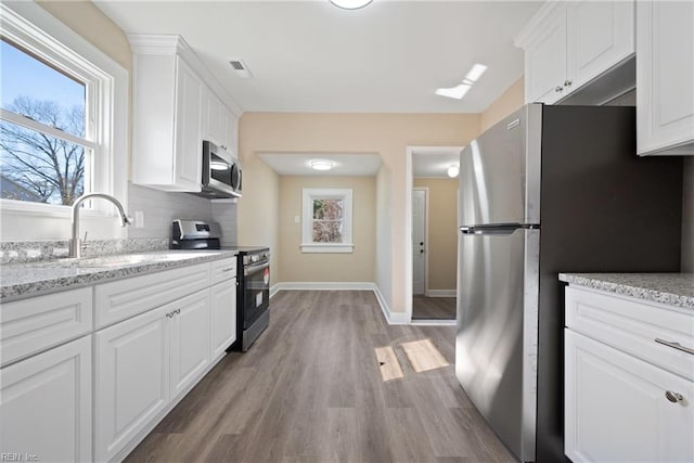 kitchen featuring appliances with stainless steel finishes, white cabinetry, decorative backsplash, light hardwood / wood-style floors, and light stone countertops