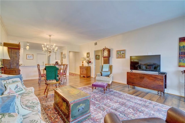 living room with crown molding, an inviting chandelier, and light wood-type flooring