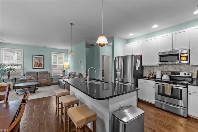 kitchen with sink, white cabinetry, decorative light fixtures, appliances with stainless steel finishes, and an island with sink