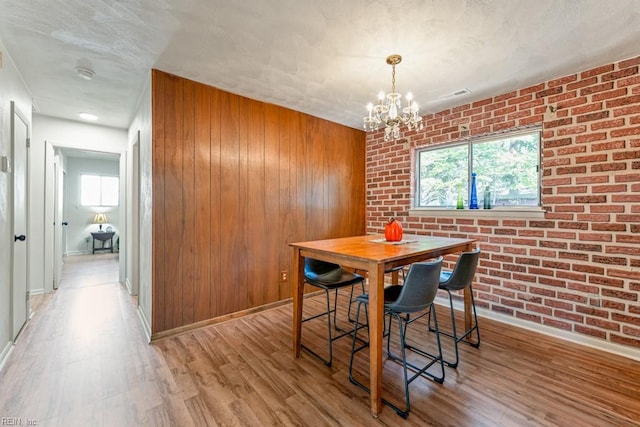 dining area with brick wall, a notable chandelier, wooden walls, and light hardwood / wood-style flooring