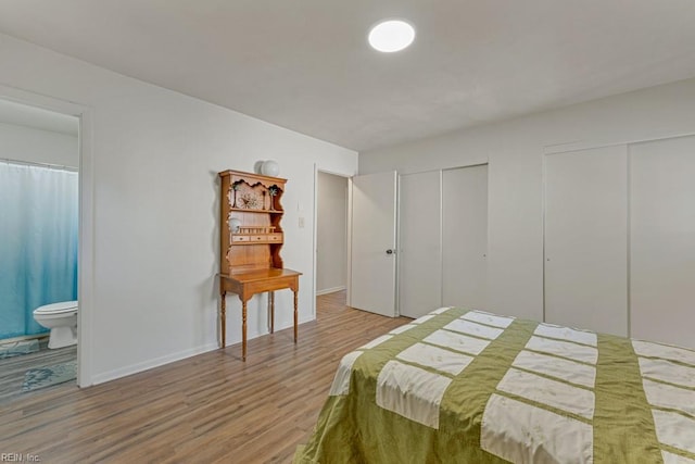 bedroom with connected bathroom, hardwood / wood-style floors, and multiple closets