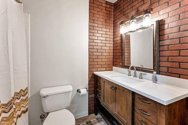 bathroom featuring vanity, brick wall, and toilet