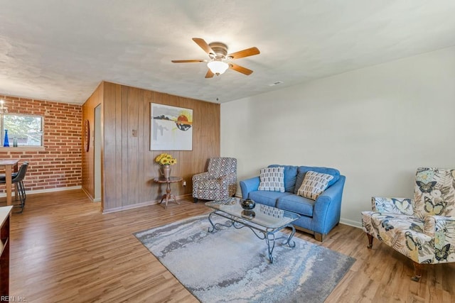 living room with ceiling fan, brick wall, and light wood-type flooring