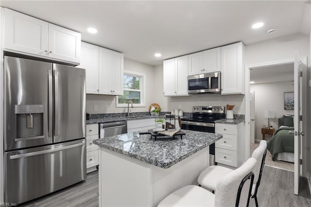 kitchen featuring light hardwood / wood-style flooring, stone counters, white cabinetry, appliances with stainless steel finishes, and a kitchen island