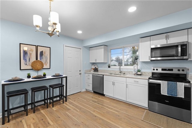 kitchen with pendant lighting, sink, appliances with stainless steel finishes, light hardwood / wood-style floors, and white cabinets