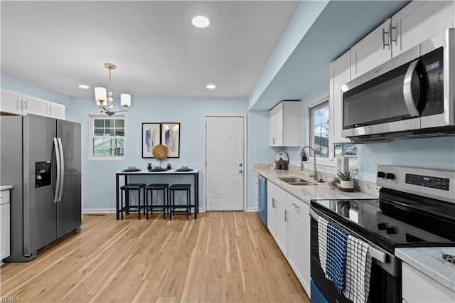 kitchen with decorative light fixtures, white cabinetry, sink, light hardwood / wood-style floors, and stainless steel appliances