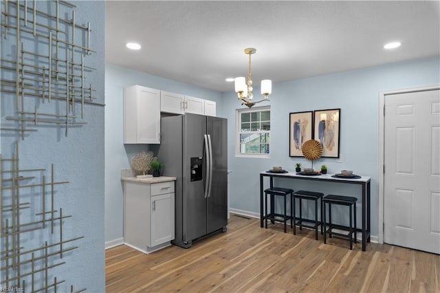 kitchen with decorative light fixtures, a chandelier, stainless steel fridge, light hardwood / wood-style floors, and white cabinets