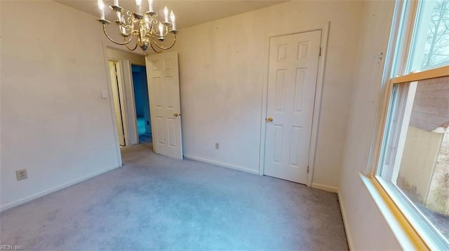 empty room featuring carpet, a chandelier, and baseboards