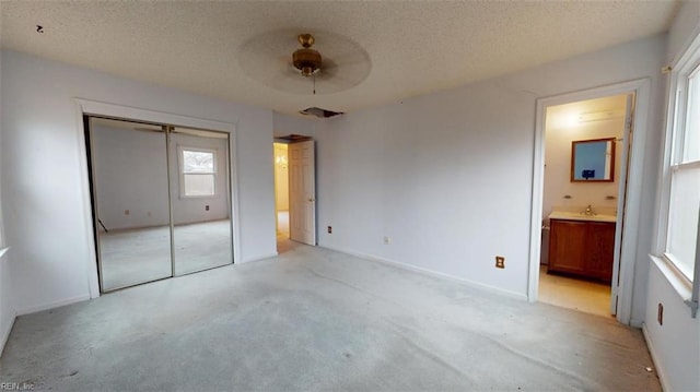 unfurnished bedroom featuring a textured ceiling, connected bathroom, light carpet, a sink, and a closet