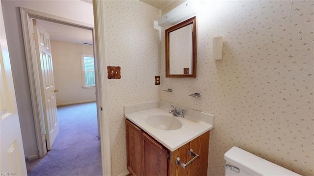 bathroom featuring vanity, toilet, and wallpapered walls