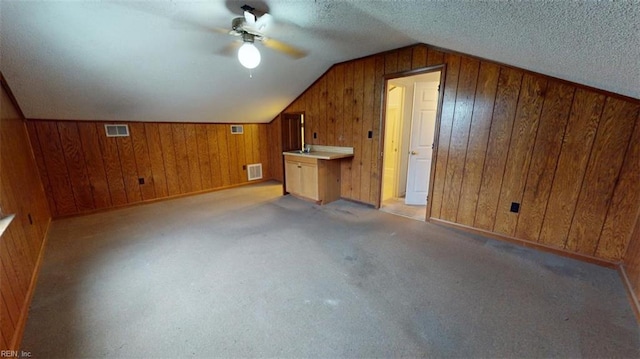 additional living space with lofted ceiling, visible vents, wood walls, and light carpet