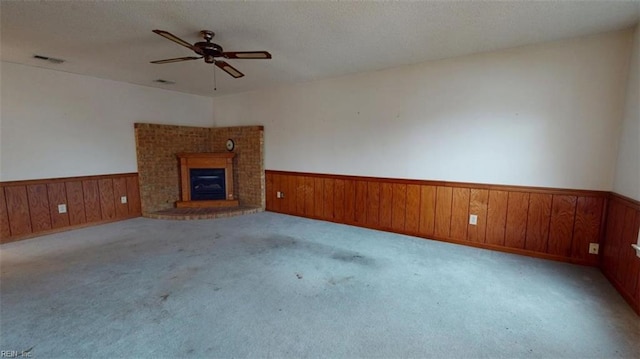 unfurnished living room featuring a wainscoted wall, ceiling fan, a brick fireplace, and visible vents