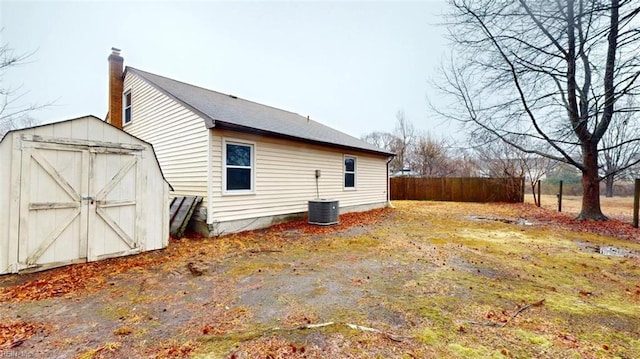 view of side of property featuring an outdoor structure, fence, central AC unit, and a shed