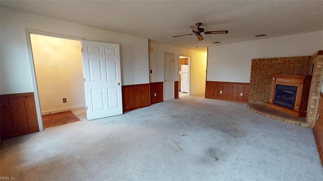 unfurnished living room with a wainscoted wall, visible vents, a brick fireplace, carpet flooring, and wood walls