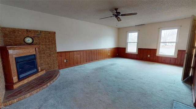 unfurnished living room with a textured ceiling, wainscoting, a fireplace, and carpet