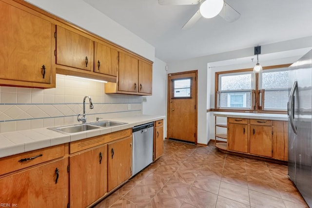 kitchen with sink, appliances with stainless steel finishes, tile counters, pendant lighting, and decorative backsplash