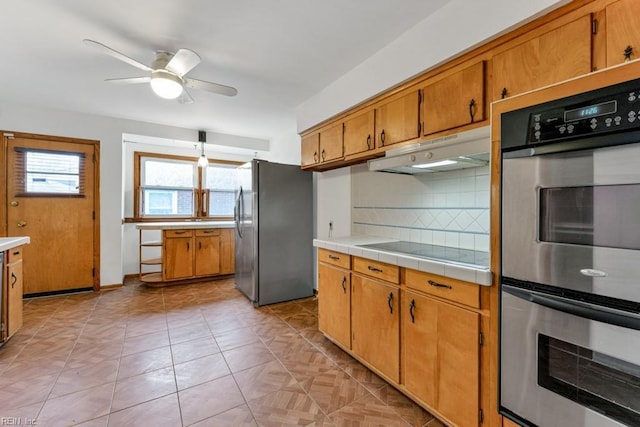 kitchen with stainless steel appliances, tile counters, ceiling fan, and decorative backsplash