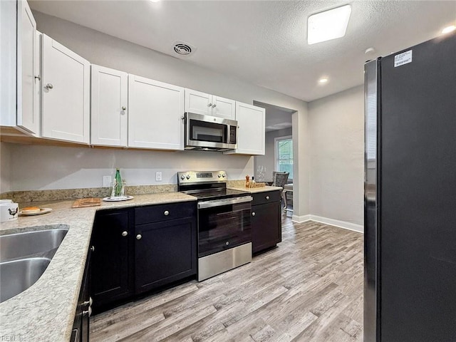 kitchen with sink, light hardwood / wood-style flooring, appliances with stainless steel finishes, white cabinetry, and a textured ceiling