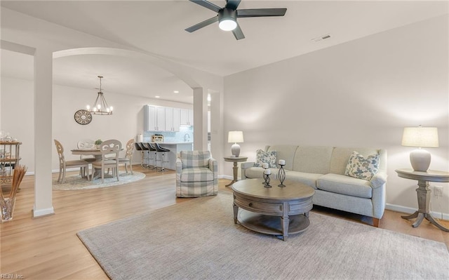 living room featuring ceiling fan with notable chandelier and light hardwood / wood-style flooring