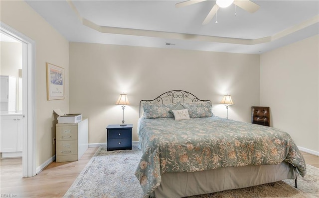 bedroom with a raised ceiling, connected bathroom, and light hardwood / wood-style floors