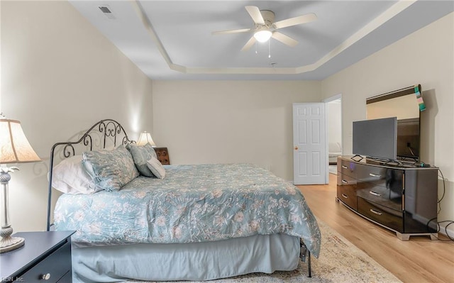 bedroom with light hardwood / wood-style floors, a raised ceiling, and ceiling fan