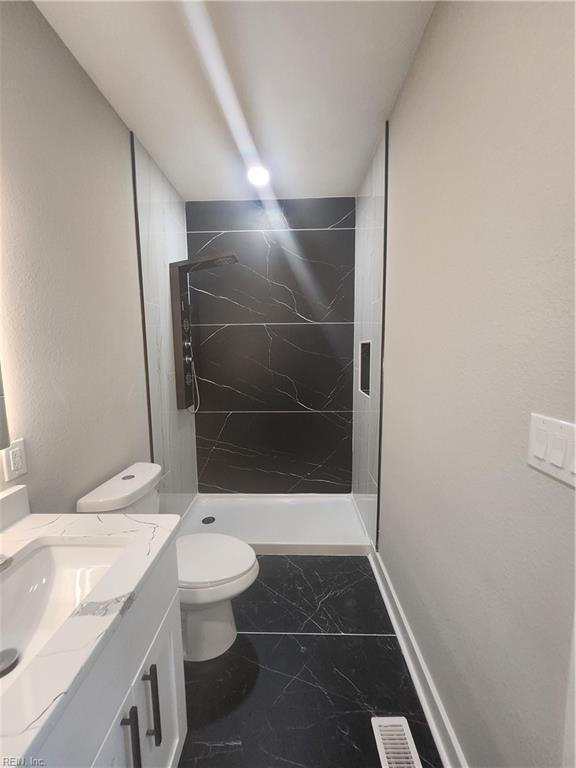 bathroom featuring a tile shower, vanity, and toilet