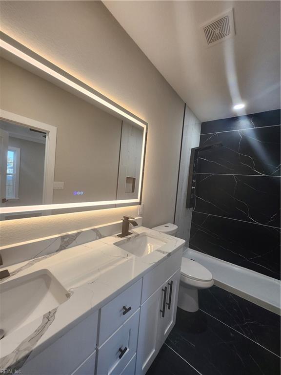 bathroom featuring tiled shower, vanity, and toilet