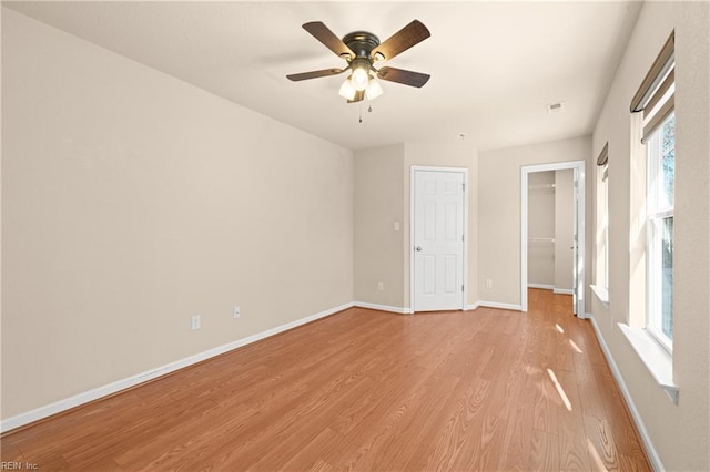 unfurnished bedroom featuring a spacious closet, light hardwood / wood-style floors, a closet, and ceiling fan