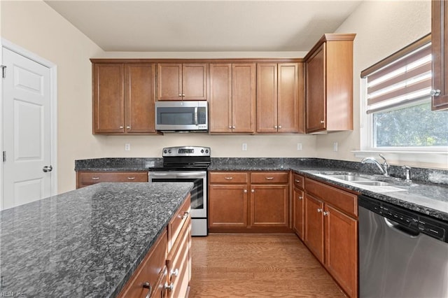 kitchen with dark stone countertops, sink, light hardwood / wood-style flooring, and stainless steel appliances