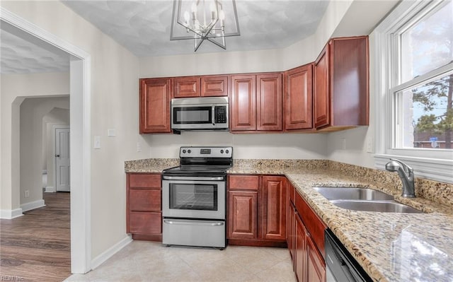 kitchen featuring sink, an inviting chandelier, light tile patterned floors, stainless steel appliances, and light stone countertops