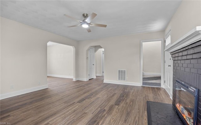 unfurnished living room with a brick fireplace, dark hardwood / wood-style floors, and ceiling fan