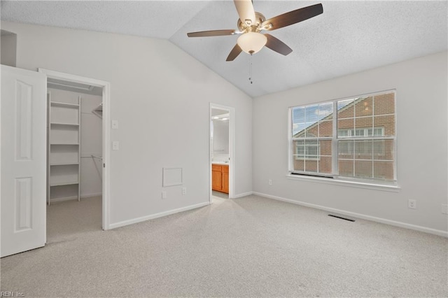 unfurnished bedroom with a walk in closet, light colored carpet, a textured ceiling, and vaulted ceiling