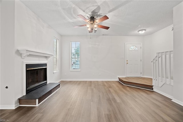 unfurnished living room featuring ceiling fan, hardwood / wood-style floors, and a textured ceiling