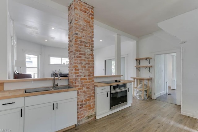 kitchen featuring white cabinetry, wooden counters, stainless steel oven, black electric cooktop, and light hardwood / wood-style flooring