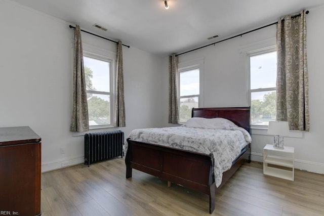 bedroom with multiple windows, radiator heating unit, and light hardwood / wood-style floors