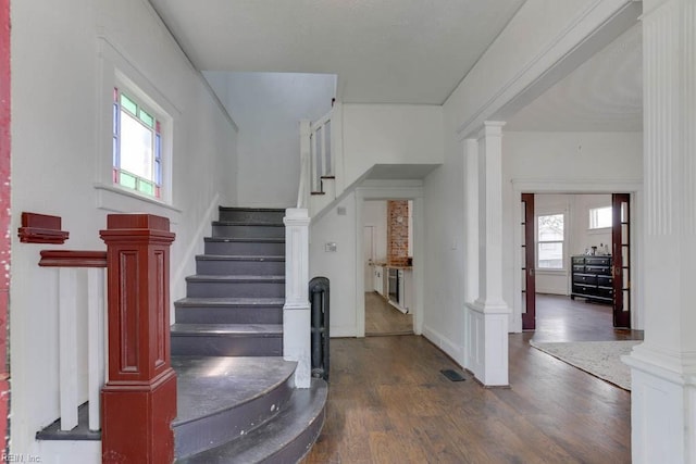 stairs with hardwood / wood-style floors, decorative columns, and a healthy amount of sunlight