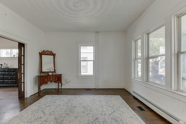 empty room featuring baseboard heating, a healthy amount of sunlight, and dark hardwood / wood-style flooring